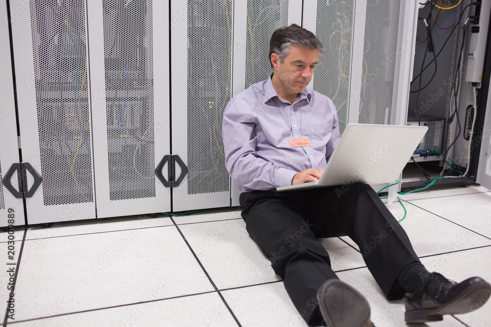 Poster Man sitting on floor using laptop to check the servers