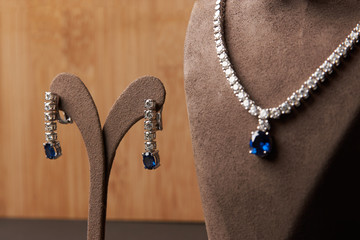 Close-up of women's platinum necklace and earrings with a diamond and blue precious sapphire stone . Luxury female jewelry - obrazy, fototapety, plakaty
