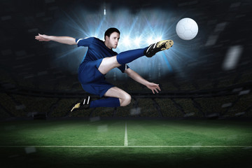 Fototapeta na wymiar Football player in blue kicking in a football pitch under spotlights