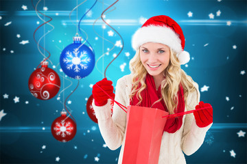 Happy festive blonde with shopping bag against hanging christmas decorations 