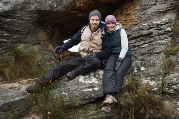 Naklejka na ściany i meble Smiling young couple sitting on rock while on a hike
