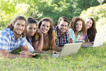 Fototapeta na wymiar Smiling friends in the park using tablet pc and laptop