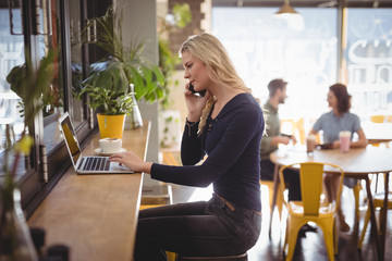 Young blond woman talking on mobile phone while using laptop