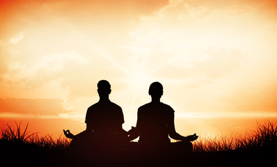 Attractive couple in white meditating in lotus pose against orange sunrise