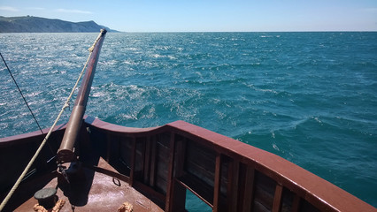 The ship sails along the sea along the high bank. The bright sun illuminates the bowsprit on the...