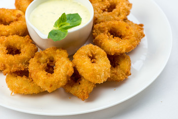 Squid rings fried in batter with white sauce on white plate on white background