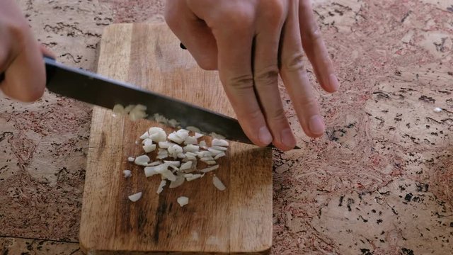 Man cuts garlic on a wooden board. Close-up man's hands.