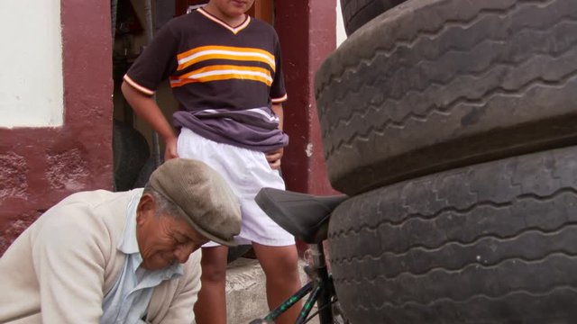 Boy watching old man repairing bike in Ecuador