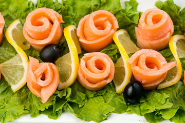 salmon snack on lettuce leaf with lemon and olives on white plate on white background