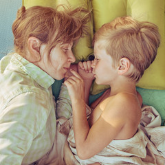 Cute little boy resting with his mom and lying outdoor on mat, image with toning and square aspect...