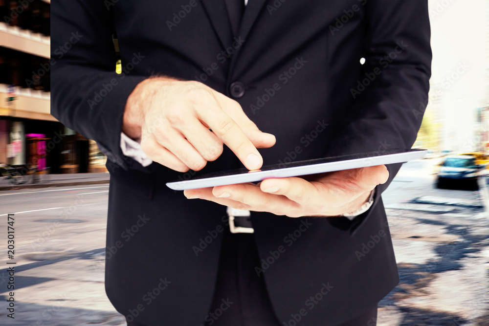 Wall mural Mid section of a businessman touching digital tablet against new york street