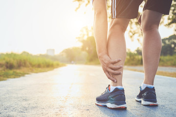 Injury from workout concept : Asian man use hands hold on his ankle while running on road in the park. Focus on ankle.