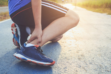 Injury from workout concept : Asian man use hands hold on his ankle while running on road in the...
