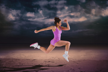 Fit brunette running and jumping against dark cloudy sky