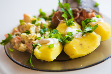 Boiled potatoes under sour cream, red fish, salad sprinkled with parsley on a plate of dark glass