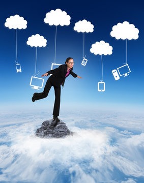 Businesswoman Stepping And Balancing Against Mountain Peak Through The Clouds