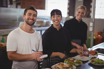 Portrait of waiter with female chefs standing in kitchen