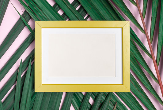 Top view blank yellow photo frame on green palm leaf on pastel pink table top background.Summer vacation backdrop.Mock up for display design and text