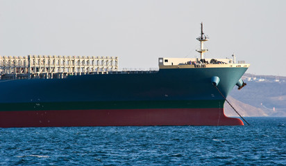 The bow of a huge container ship standing at anchor in the roadstead.