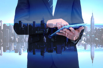 Businessman touching his tablet pc  against mirror image of city skyline