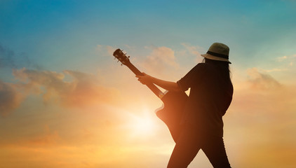 Guitarist playing acoustic guitar on the colorful cloudscape sunset background