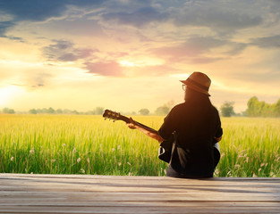 Woman playing acoustic guitar on the field rural sunset background