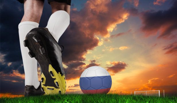 Composite image of football boot kicking russia ball against green grass under dark blue and orange sky