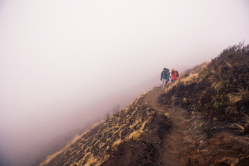 Hikers couple with backpacks walking on top of mountain in fog above clouds