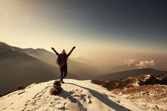 Female Traveller relaxing above clouds on top of snow high mountain and enjoying view of valley, freedom travel concept, nepali style hat, sunrise