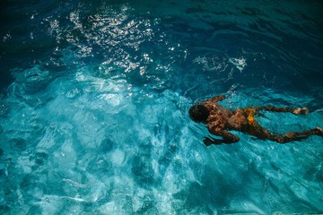 Fototapeta na wymiar Young sporty man swimming in blue water of pool. Dark skin, mixed race, black African hairstyle.