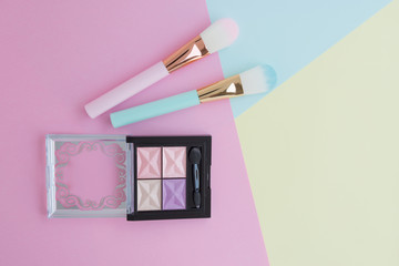 Flat lay of creative female decorative cosmetic for pink and blue cheek brush and eyeshadow palette on the colorful background with copy space