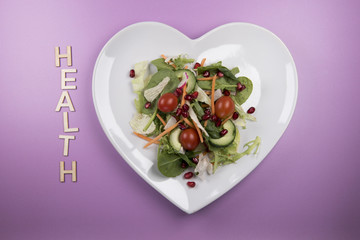 Traditional salad on a heart shaped plate with the word health in wooden letters 