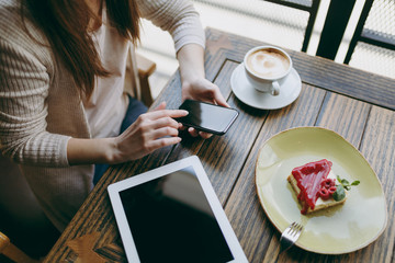 Close up woman in coffee shop with tablet pc computer cup of cappuccino cake relax in restaurant during free time. Female holding mobile phone with blank empty screen rest in cafe. Lifestyle concept.