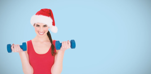 Festive fit brunette holding dumbbells against blue background