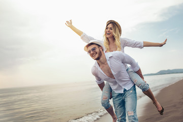 Happy couple in love on beach summer vacations. Joyful girl piggybacking on young boyfriend having fun. - obrazy, fototapety, plakaty