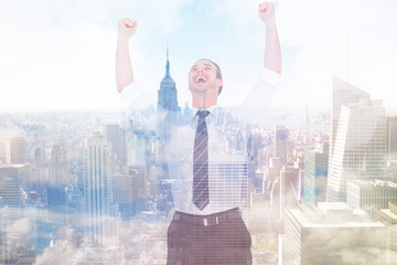 Handsome businessman cheering with arms up against city skyline