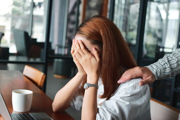 Hand's of colleague comforting depressed sad Asian woman with hands on face crying on the workplace in office.