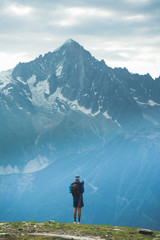 A hiker standing at the top of a mountain pass looking across a valley to a mountain peak - 203043606