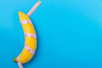 Yellow banana with measurement tape on blue background. Men penis size concept with empty free...