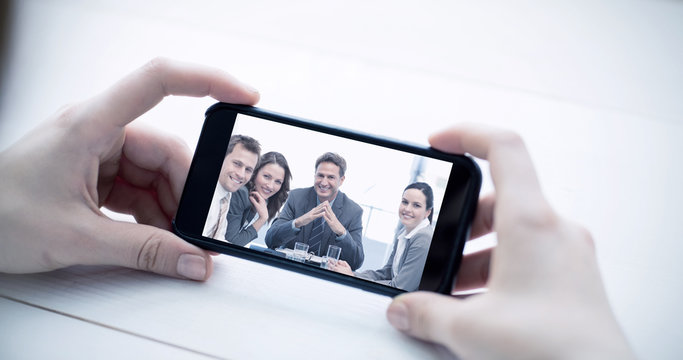 Cropped image of man holding smartphone against portrait of a positive manager with his team
