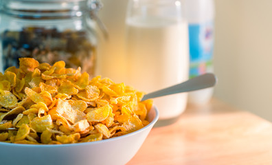 Bowl of cereal with spoon put on wood table near granola in glass container and one glass of milk. Calcium food breakfast for children before go to school in the morning. Cornflakes and milk concept
