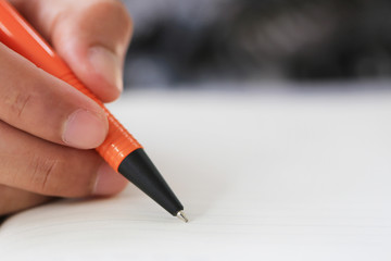 Hand of businessman hold a orange pen writing to the note on paper book.