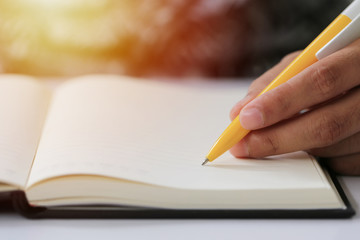 Hand of businessman hold a yellow pen writing to the note on paper book.