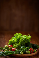 Vegetarian still life of fresh vegetables on wooden plate over rustic background, close-up, flat lay.