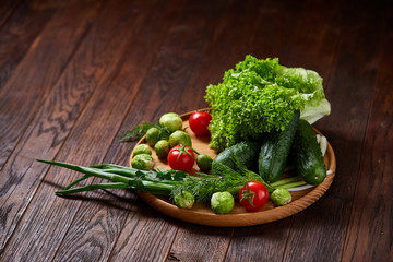 Vegetarian still life of fresh vegetables on wooden plate over rustic background, close-up, flat lay.