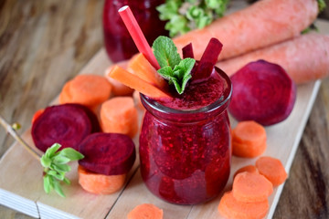 Red smoothie made of carrot and beet is decorated with pieces of the vegetables and mint in a glass jar