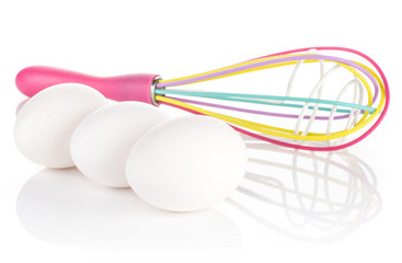 Three white chicken eggs and silicon colourful balloon whisk isolated on white background.