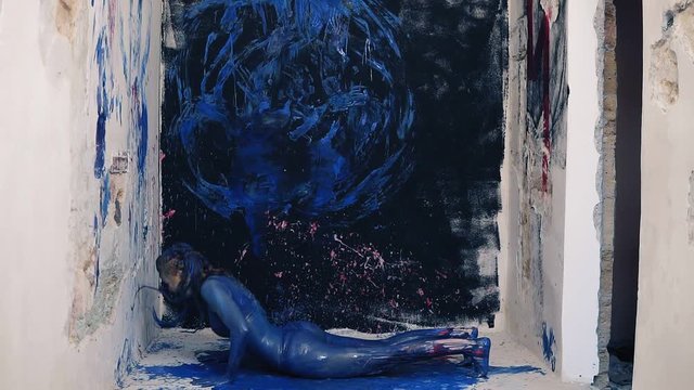 Young attractive woman painted in blue colour doing exercises in the colorful room. Front footage