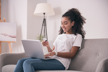 Modern device. Pleasant young woman holding her laptop while making an online payment