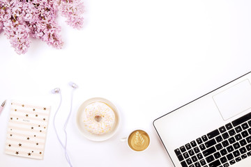 Feminine desktop close up, laptop computer keyboard, cup of coffee and donut, lilac flowers. Minimal cropped flat lay composition, notebook, cappuccino, purple bouquet, white background. Copy space.